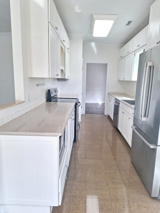 kitchen with white cabinetry, appliances with stainless steel finishes, built in desk, and light stone countertops