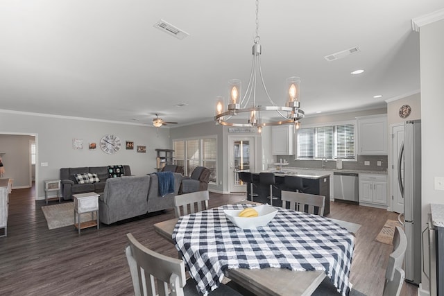 dining room with dark wood-type flooring, ornamental molding, and ceiling fan with notable chandelier