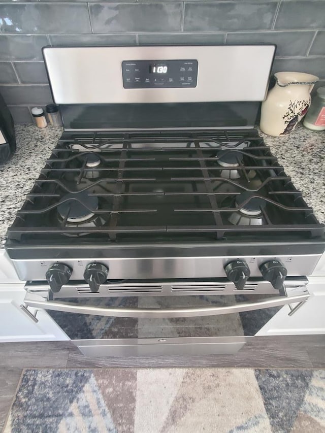 details with hardwood / wood-style flooring, stainless steel gas range, and light stone counters