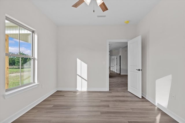 unfurnished room featuring wood finished floors, a healthy amount of sunlight, a ceiling fan, and baseboards