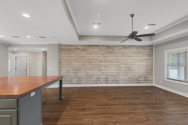 unfurnished room featuring wooden walls, dark hardwood / wood-style flooring, ceiling fan, a tray ceiling, and crown molding