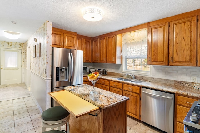 kitchen featuring stainless steel appliances, a sink, a kitchen island, a kitchen breakfast bar, and brown cabinets