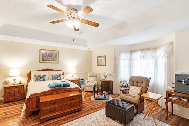 bedroom with a raised ceiling, visible vents, a ceiling fan, a textured ceiling, and wood finished floors