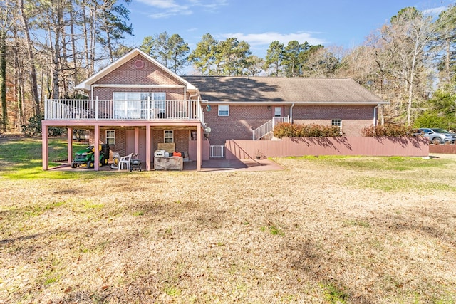 rear view of house featuring a deck, a patio, brick siding, and a lawn