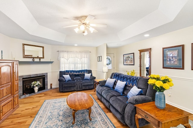 living room featuring a textured ceiling, a fireplace, a ceiling fan, light wood-type flooring, and a raised ceiling