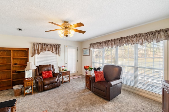 sitting room with a ceiling fan, visible vents, light colored carpet, and a textured ceiling