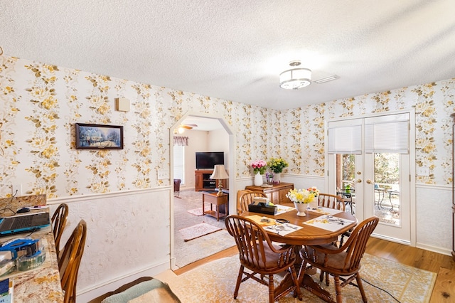 dining area with arched walkways, a wainscoted wall, a textured ceiling, wood finished floors, and wallpapered walls