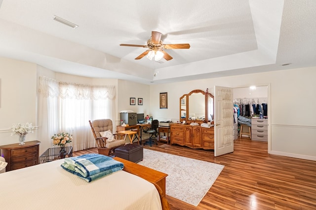 bedroom with wood finished floors, a spacious closet, a tray ceiling, a textured ceiling, and a closet