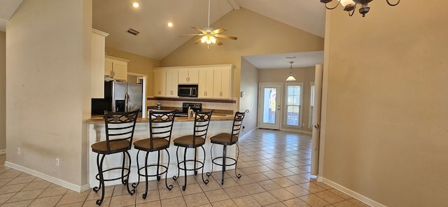 kitchen featuring stainless steel appliances, light tile patterned floors, white cabinets, and high vaulted ceiling