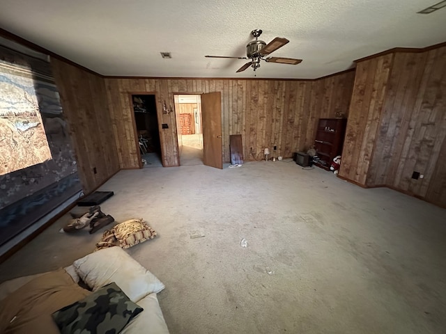 unfurnished living room with ornamental molding, a textured ceiling, ceiling fan, carpet floors, and wood walls