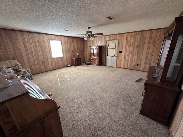 interior space with light carpet, a textured ceiling, ceiling fan, and wood walls