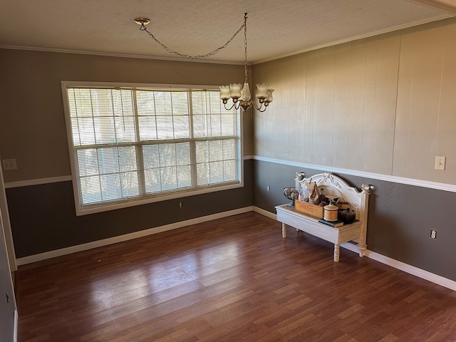 unfurnished dining area featuring hardwood / wood-style floors, an inviting chandelier, crown molding, wooden walls, and a textured ceiling