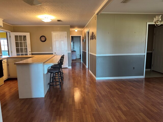 kitchen featuring dark wood-type flooring, wood counters, crown molding, a breakfast bar, and white cabinets