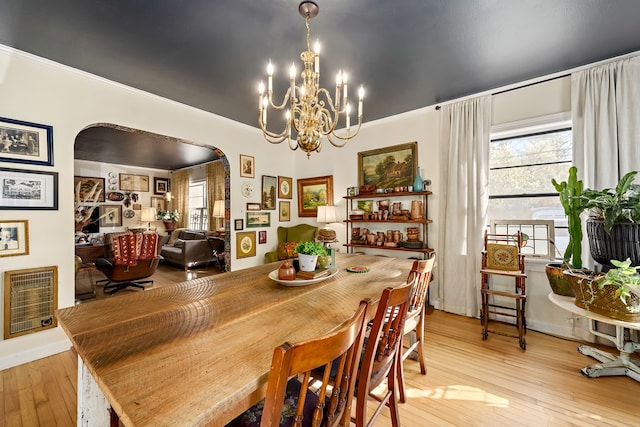 dining space featuring arched walkways, ornamental molding, and light wood-style floors