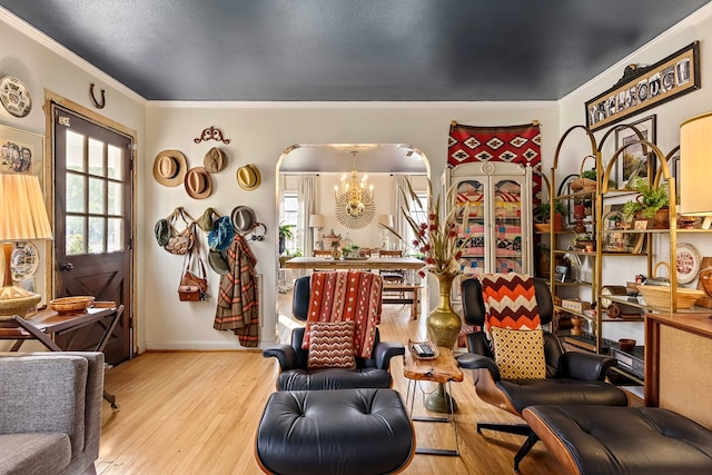 sitting room with arched walkways, wood finished floors, baseboards, ornamental molding, and an inviting chandelier