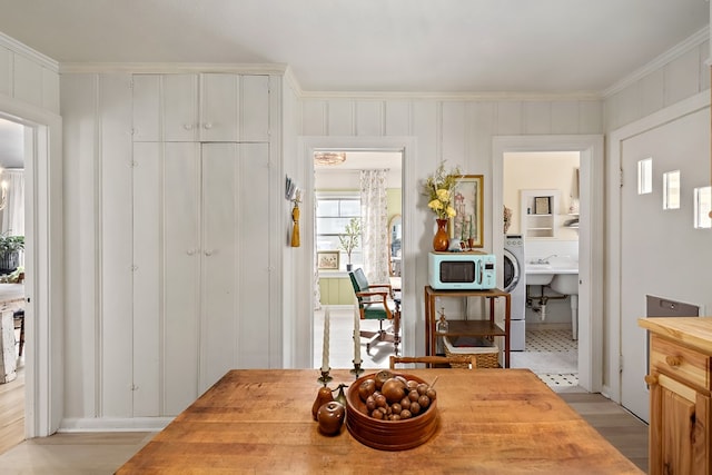 dining area with ornamental molding, light wood-style floors, washer / dryer, and a decorative wall