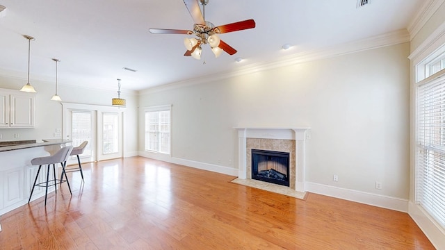 unfurnished living room with a tiled fireplace, ornamental molding, ceiling fan, and light wood-type flooring