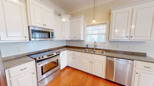 kitchen with pendant lighting, sink, crown molding, white cabinetry, and stainless steel appliances