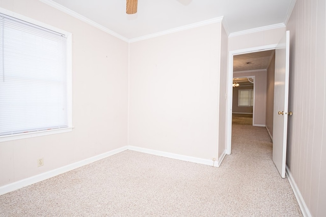 spare room featuring light colored carpet, crown molding, baseboards, and ceiling fan