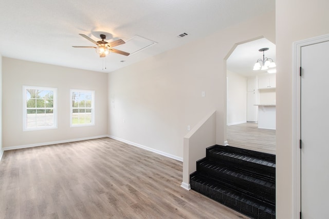 spare room with arched walkways, light wood-style flooring, ceiling fan with notable chandelier, visible vents, and baseboards