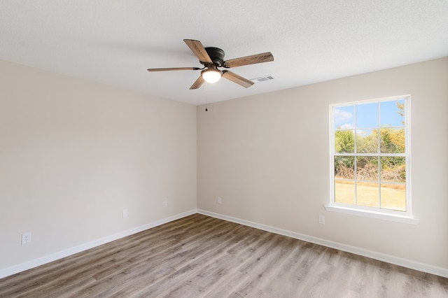 empty room featuring a textured ceiling, ceiling fan, light wood-style flooring, visible vents, and baseboards