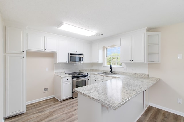 kitchen featuring stainless steel appliances, a peninsula, a sink, white cabinetry, and light countertops