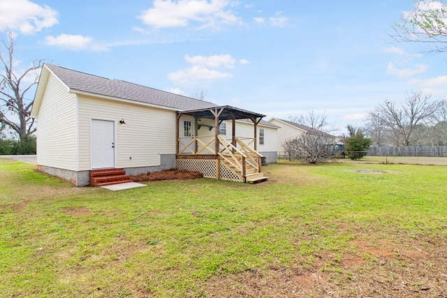 rear view of property featuring entry steps, a shingled roof, fence, and a yard