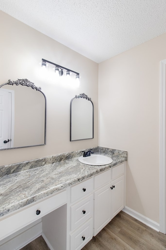 bathroom with a textured ceiling, baseboards, wood finished floors, and vanity