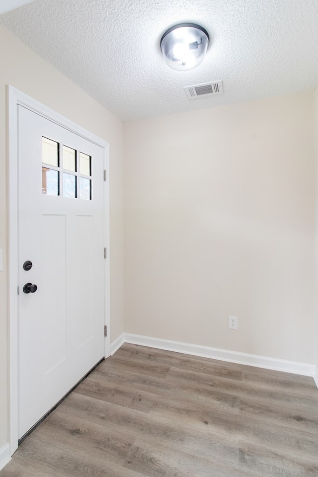 entrance foyer featuring light wood-type flooring, visible vents, a textured ceiling, and baseboards