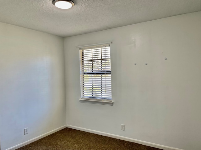 empty room with baseboards, dark colored carpet, and a textured ceiling