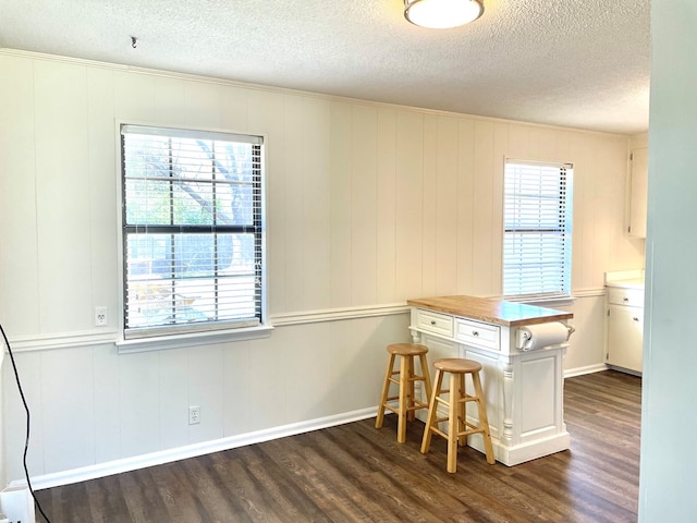 kitchen featuring dark wood-type flooring, baseboards, a kitchen bar, white cabinets, and a textured ceiling