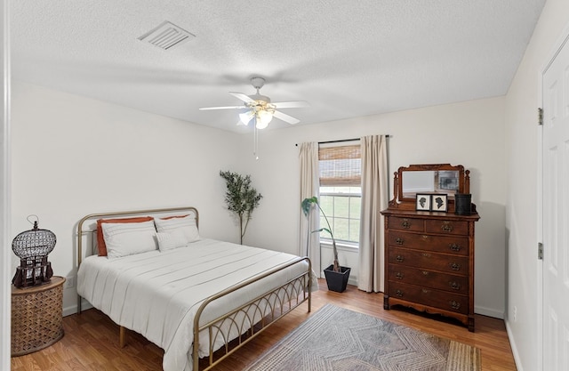 bedroom with ceiling fan, wood-type flooring, and a textured ceiling