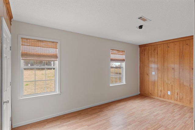 unfurnished room with a textured ceiling, light hardwood / wood-style floors, and wood walls