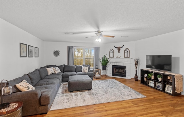 living room with wood-type flooring, a textured ceiling, ceiling fan, and a fireplace