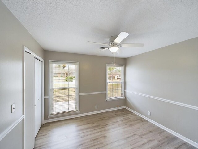 empty room with a textured ceiling, light hardwood / wood-style floors, ceiling fan, and a healthy amount of sunlight