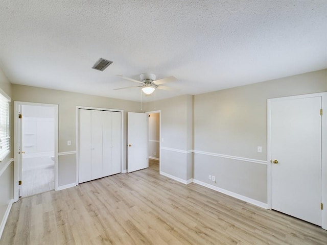 unfurnished bedroom with a textured ceiling, light wood-type flooring, ensuite bath, and ceiling fan