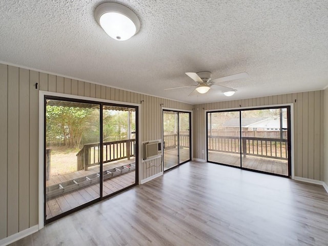 empty room featuring ceiling fan, light hardwood / wood-style flooring, a textured ceiling, and wooden walls