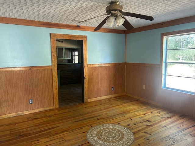 unfurnished room with plenty of natural light, wooden walls, a textured ceiling, and hardwood / wood-style flooring