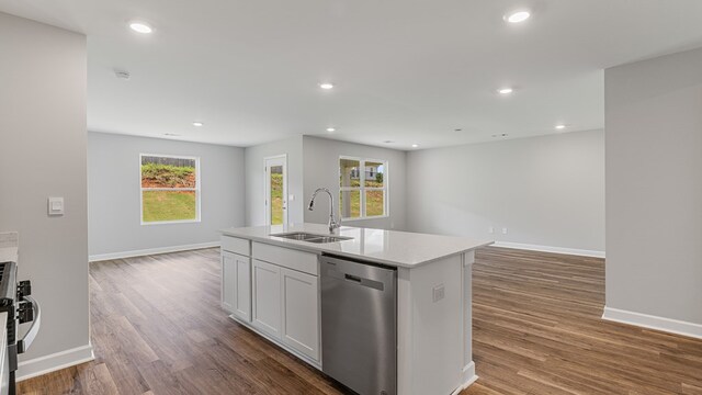 kitchen with stainless steel dishwasher, a kitchen island with sink, sink, white cabinets, and hardwood / wood-style floors