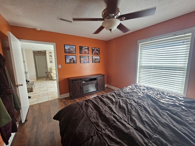 bedroom with a textured ceiling, a ceiling fan, visible vents, wood finished floors, and baseboards