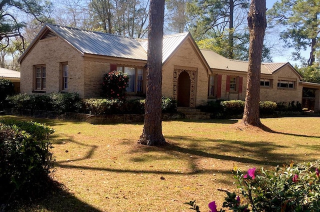 ranch-style home featuring metal roof, brick siding, and a front lawn