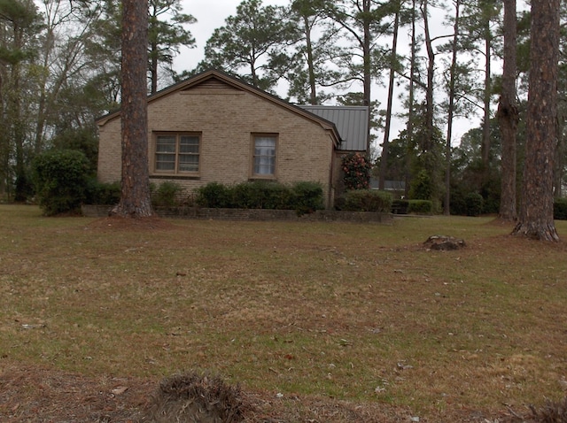 view of home's exterior featuring metal roof, brick siding, a lawn, and a standing seam roof