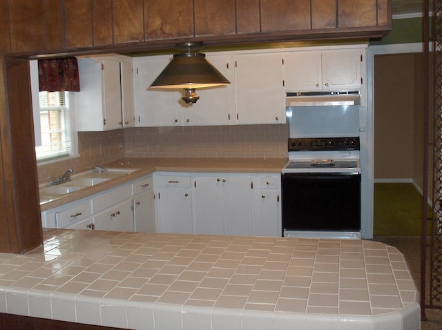 kitchen featuring electric range, under cabinet range hood, a sink, backsplash, and tile counters