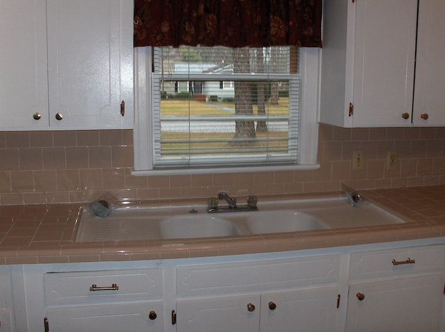 kitchen featuring decorative backsplash, tile counters, white cabinets, and a sink