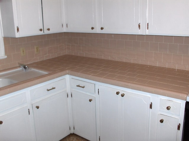 kitchen featuring tile counters, decorative backsplash, white cabinets, and a sink