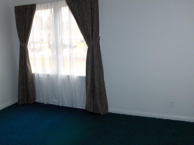 unfurnished room with baseboards and dark colored carpet