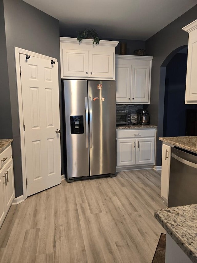 kitchen featuring light stone counters, white cabinets, stainless steel appliances, and light wood-type flooring