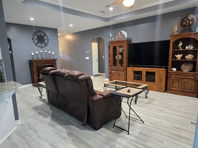 living room featuring light hardwood / wood-style floors, a raised ceiling, ceiling fan, and ornamental molding