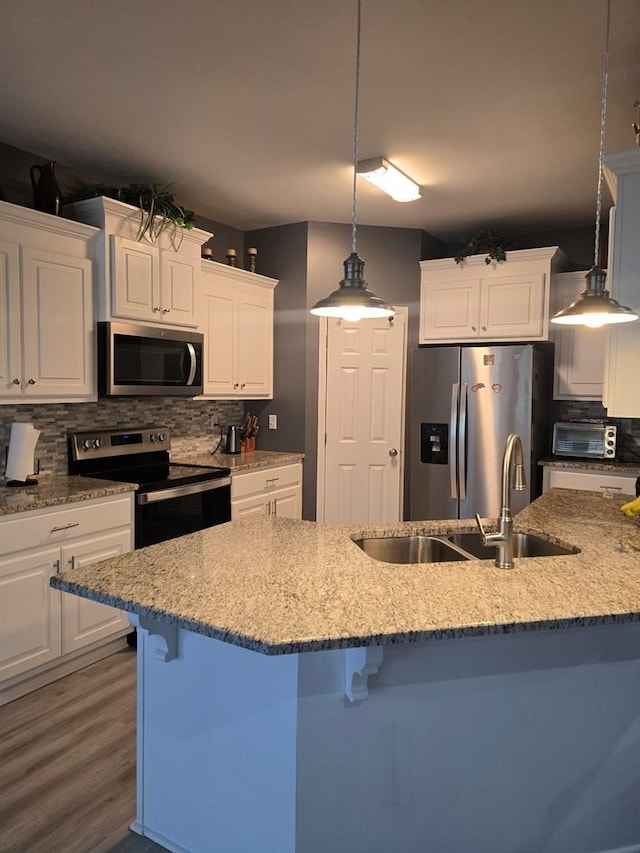 kitchen with appliances with stainless steel finishes, sink, decorative light fixtures, white cabinets, and a breakfast bar area