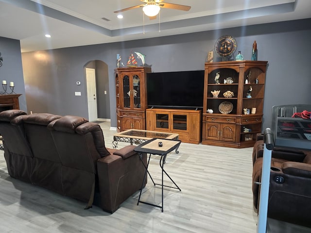 living room with ceiling fan, light hardwood / wood-style floors, a raised ceiling, and crown molding